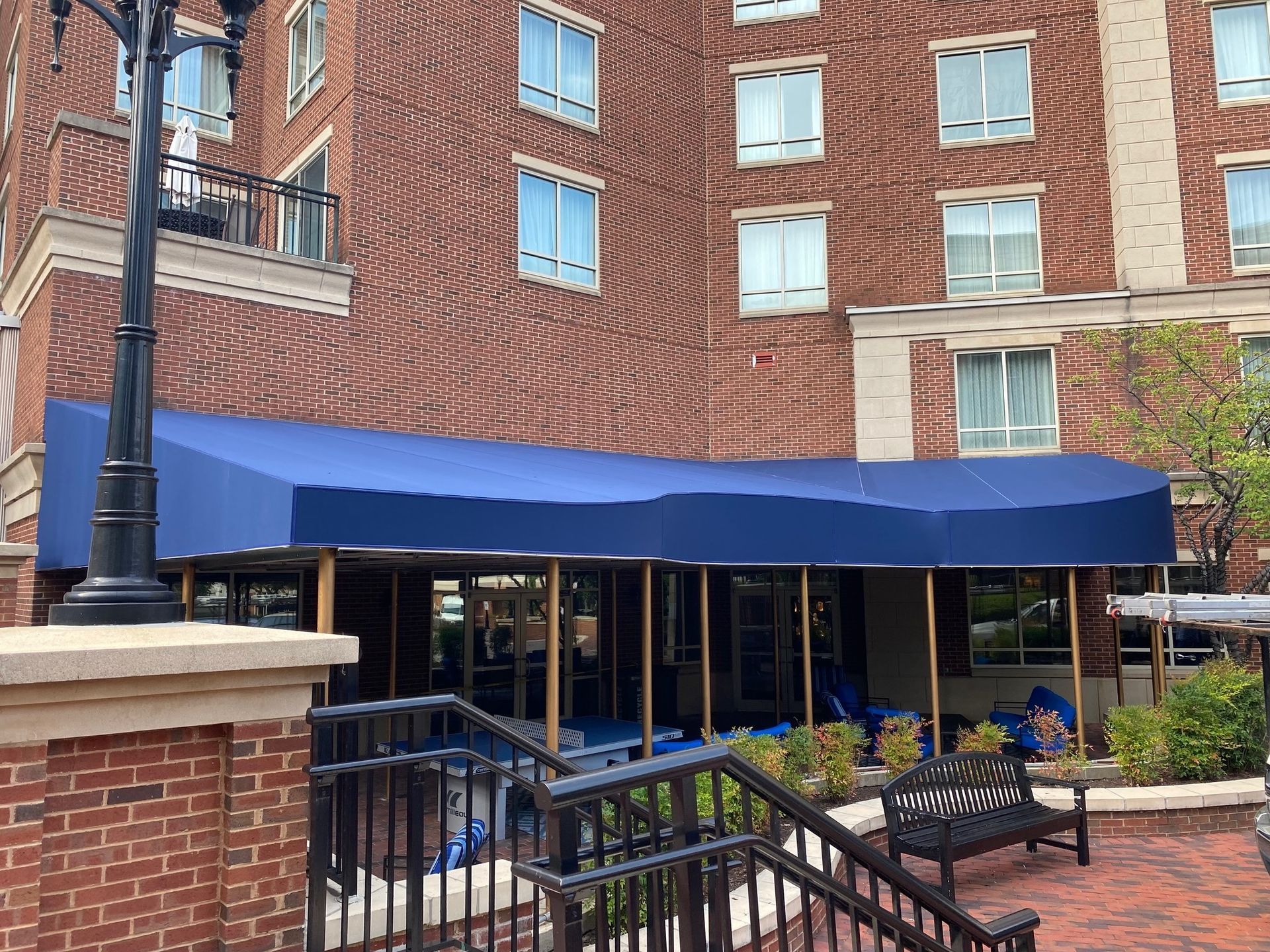 Blue awning over an outdoor patio beside a brick building with benches and a railing.