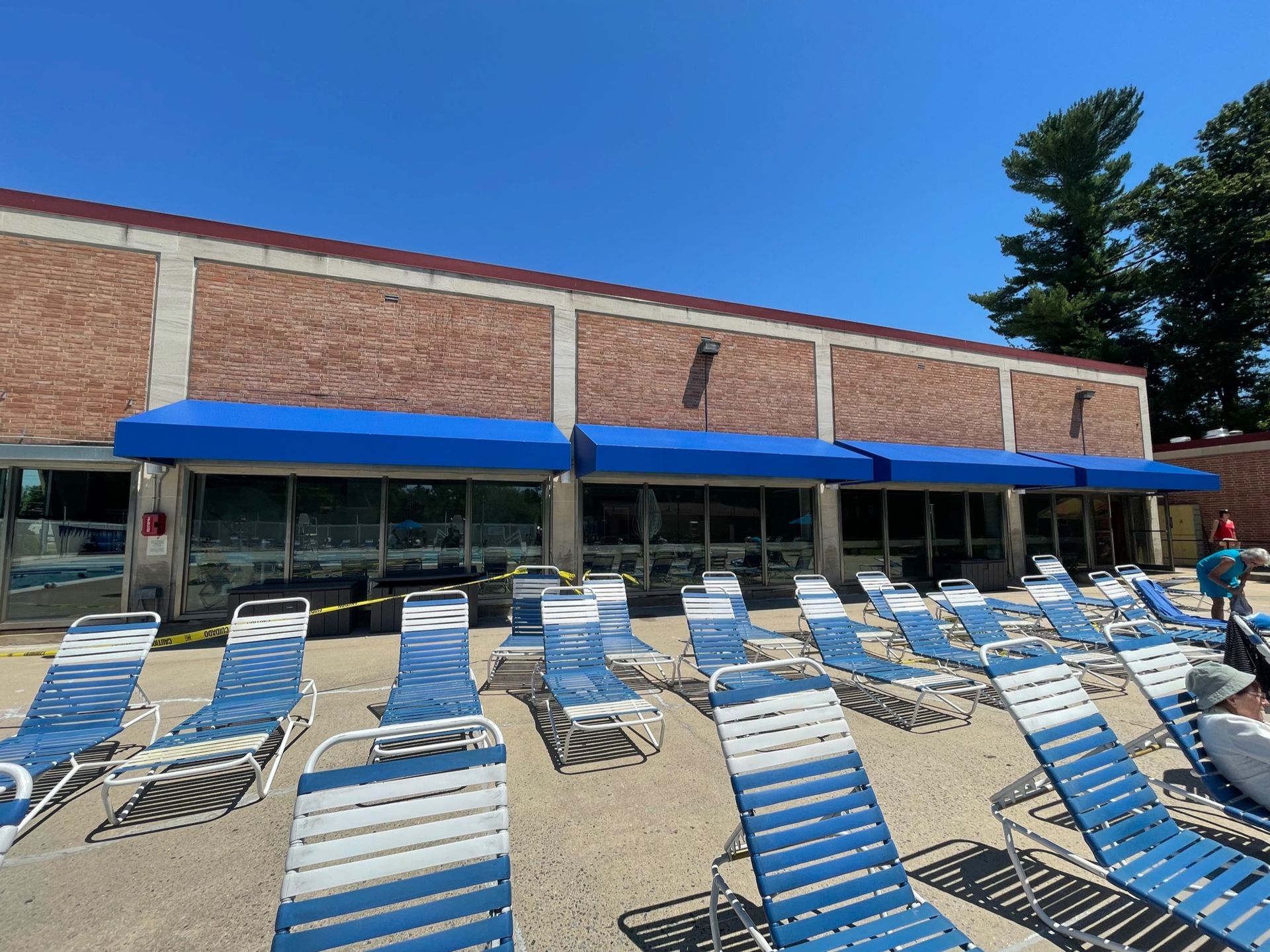 Blue-striped lounge chairs on a sunny pool deck outside a brick building with blue awnings.