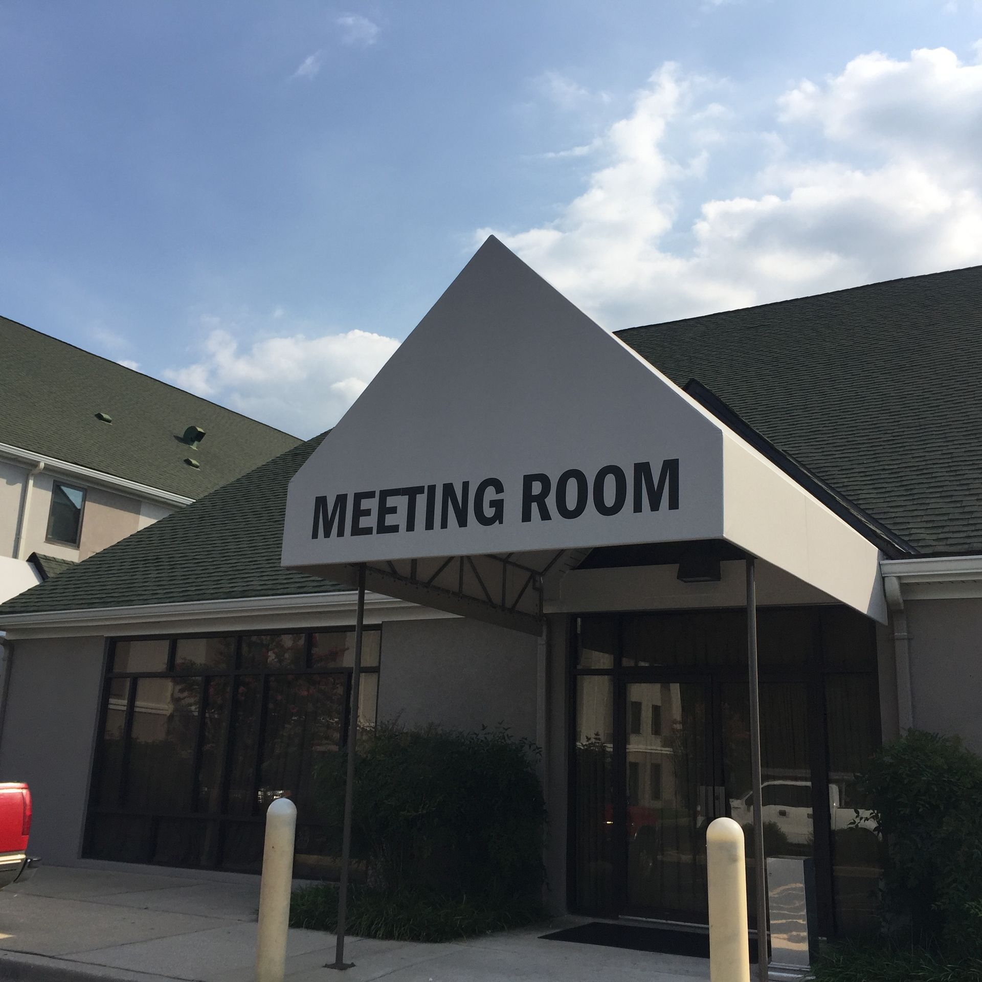 Meeting room entrance with white peaked awning and black sign on a sunny day.