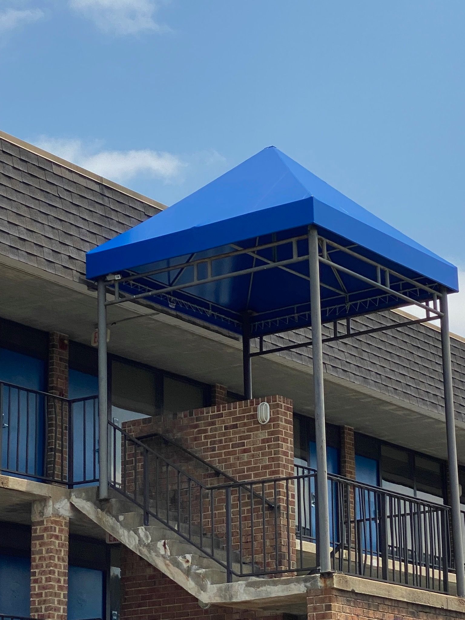 Blue awning over exterior stairway beside a brick building under a clear sky.