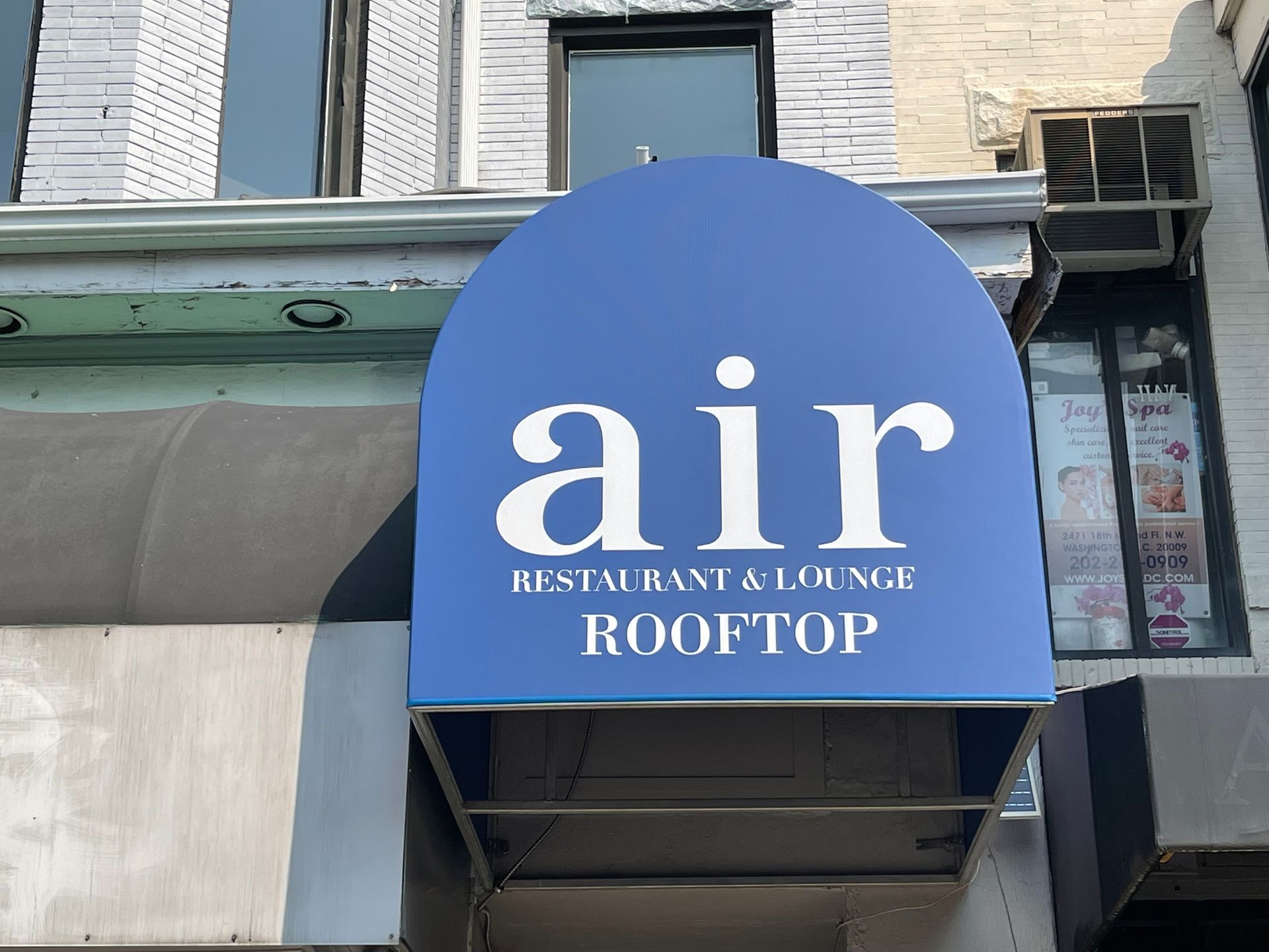 Blue awning sign reading “air restaurant & lounge ROOFTOP” above a building entrance.