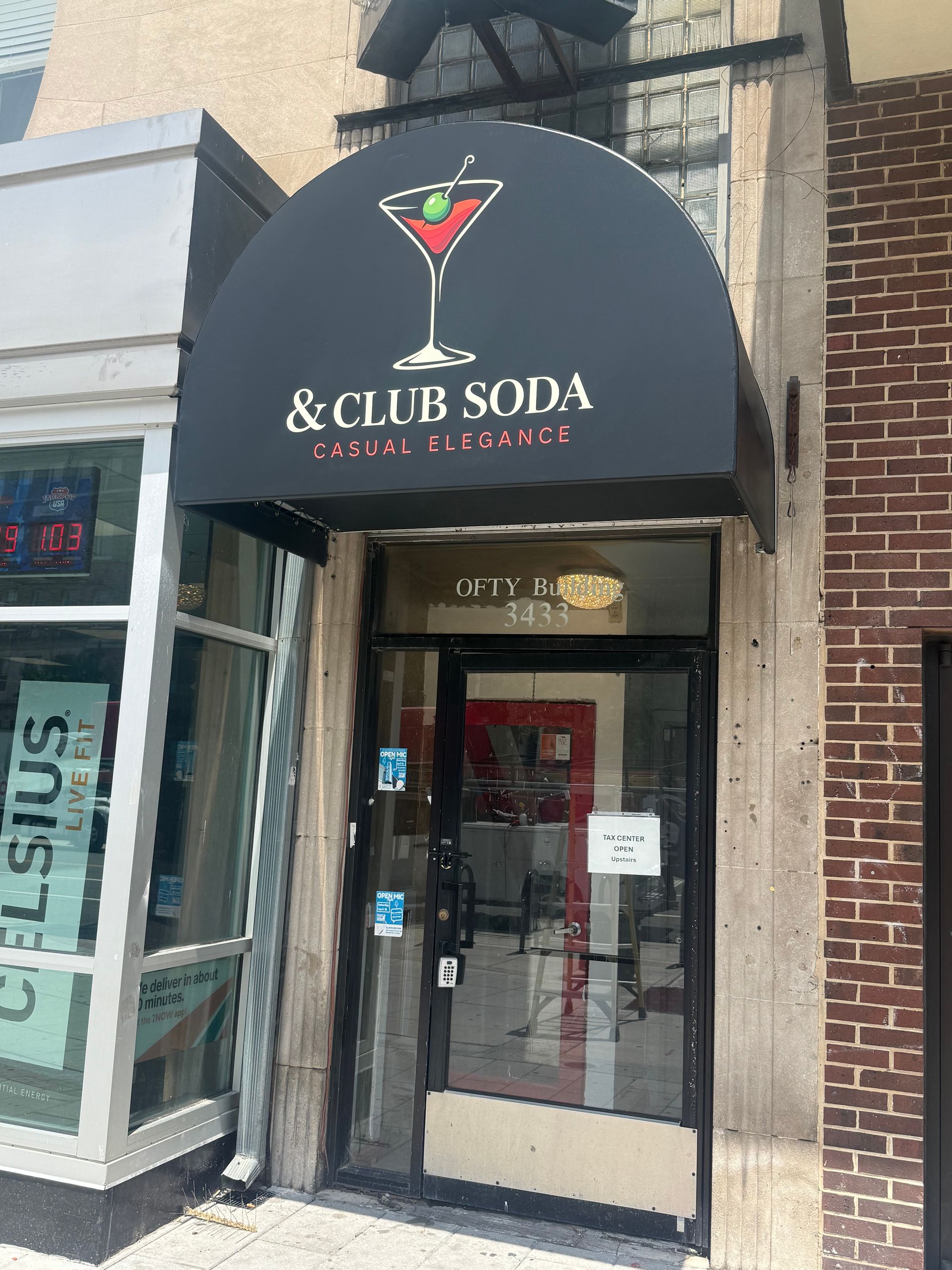 Storefront entrance with black awning reading “C&Club Soda” and glass door on a brick building.