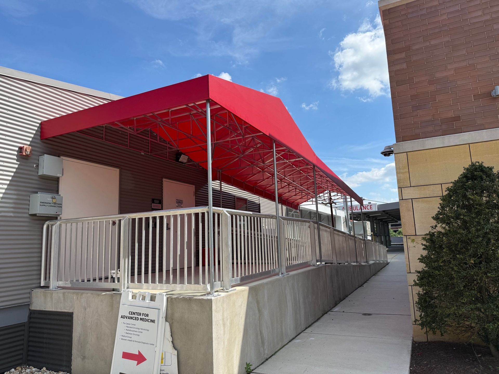 Outdoor walkway beside a building with red canopy awnings and white railings under a partly cloudy sky.