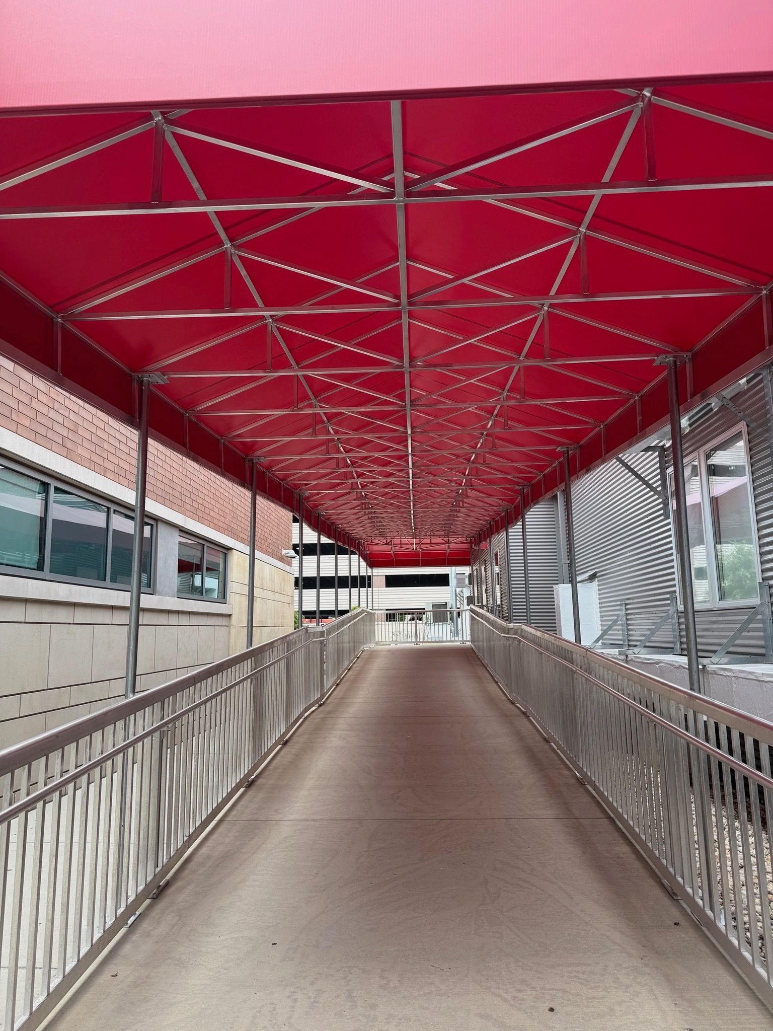 Covered pedestrian walkway with a red canopy and metal railings between buildings.