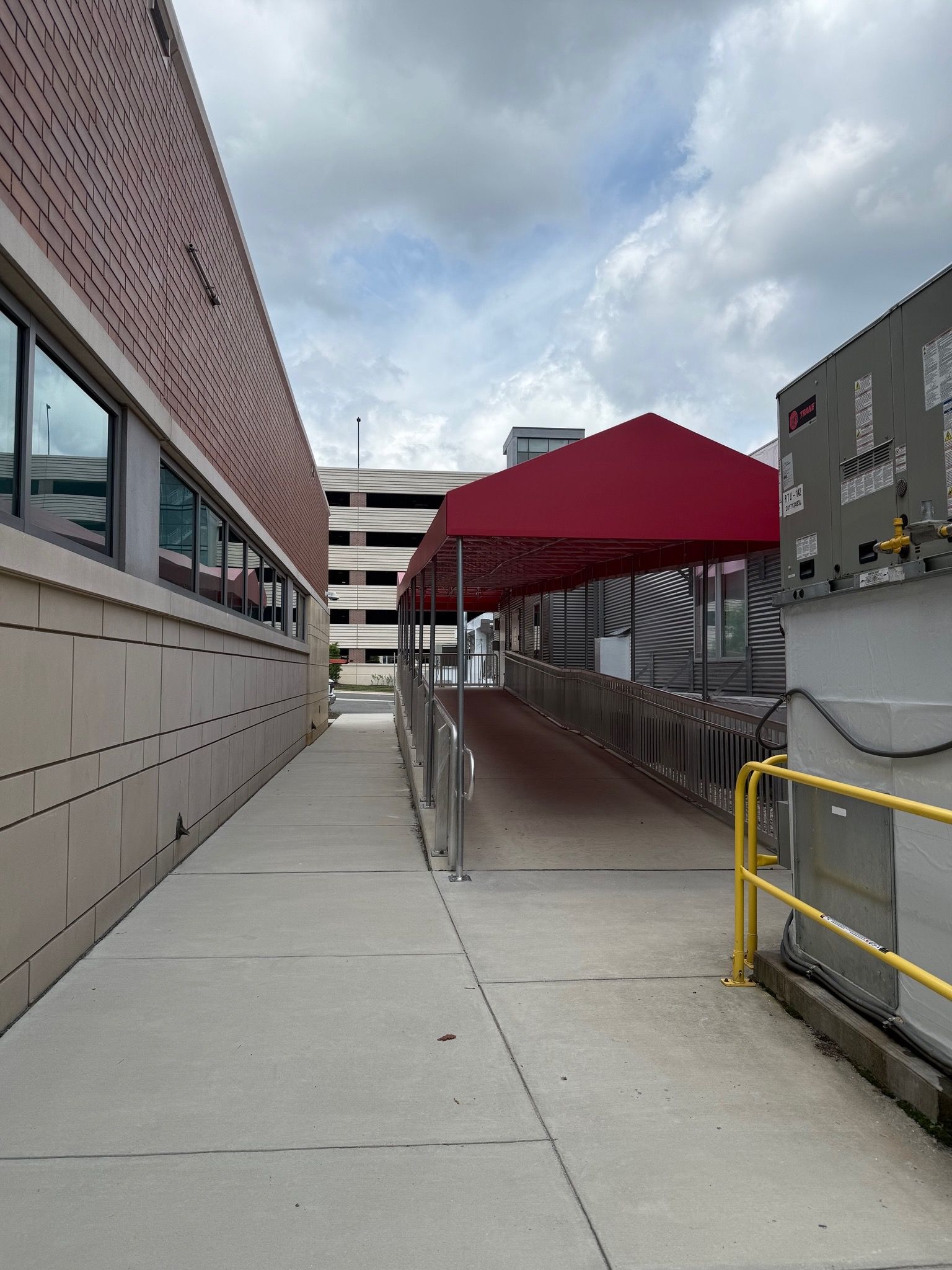 Covered walkway beside a building, with red canopy and yellow railing on a cloudy day.