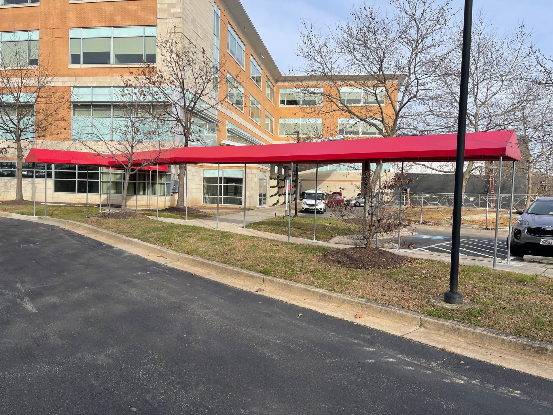 Red awning over a building entrance beside a paved driveway and leafless trees.