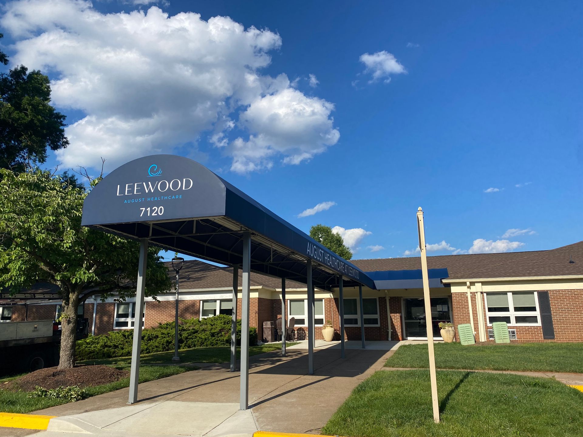 School entrance with covered walkway, blue awning, brick building, and clear sky.