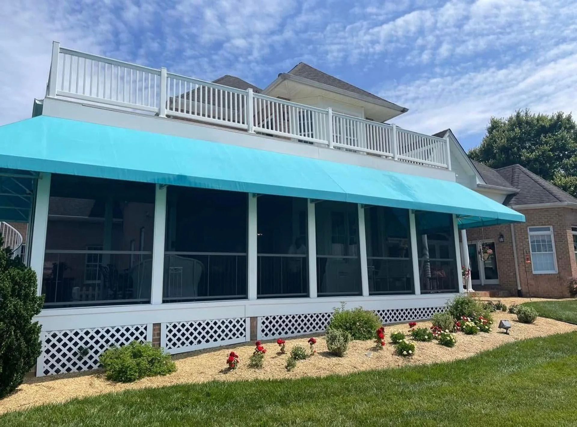 Beach house with turquoise awning, white screened porch, and rooftop deck under a blue sky
