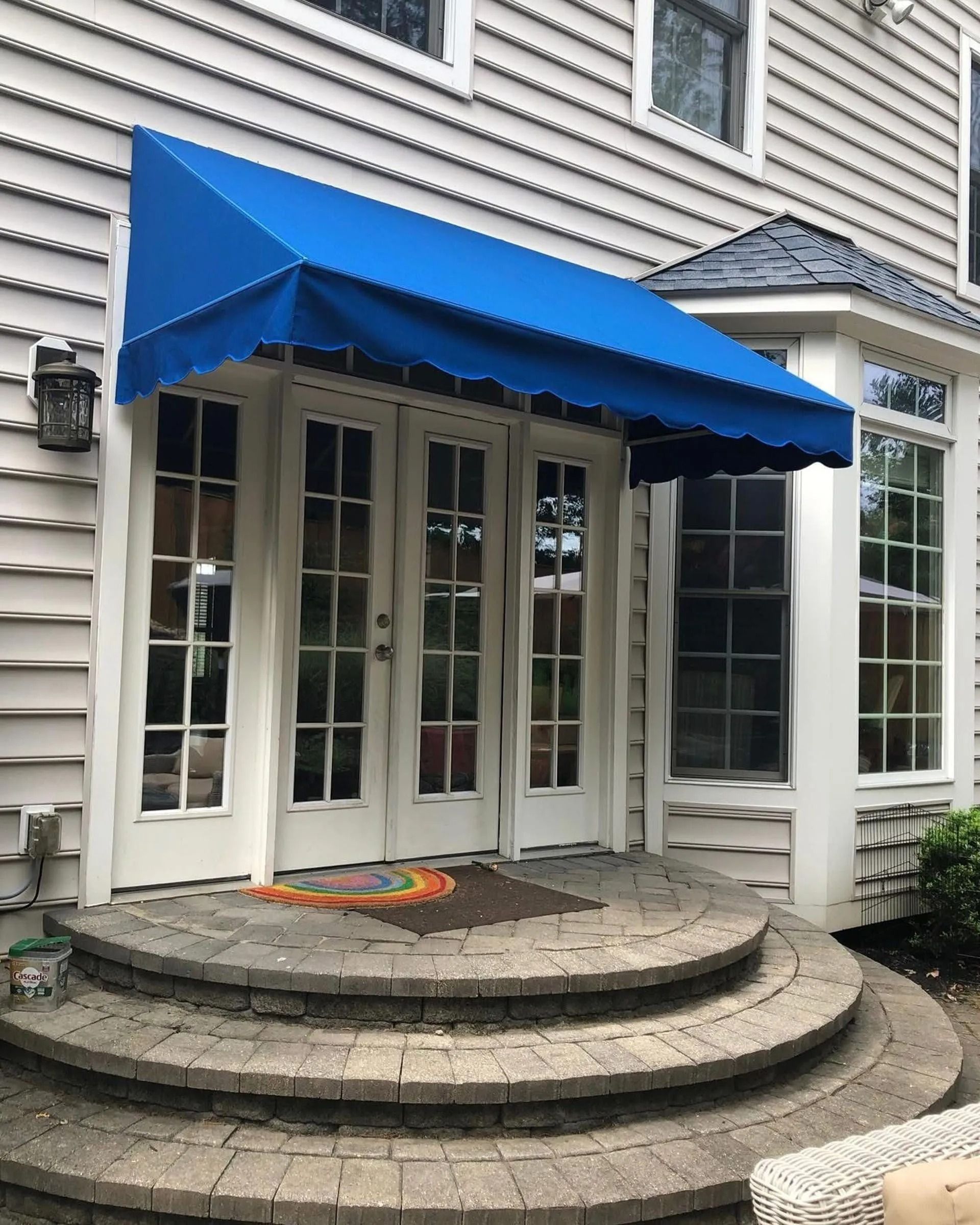 Blue awning over white French doors and curved stone steps at a house entrance