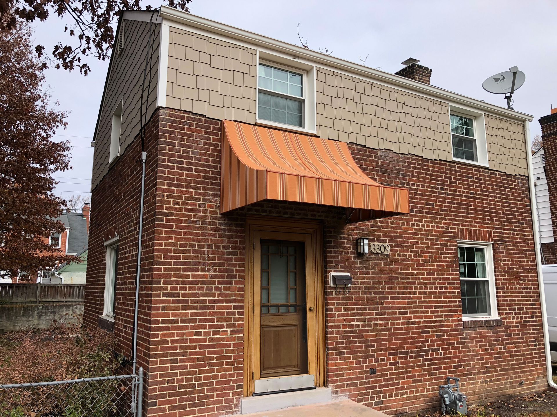 Small brick house with beige upper siding, orange awning, and a wooden front door.