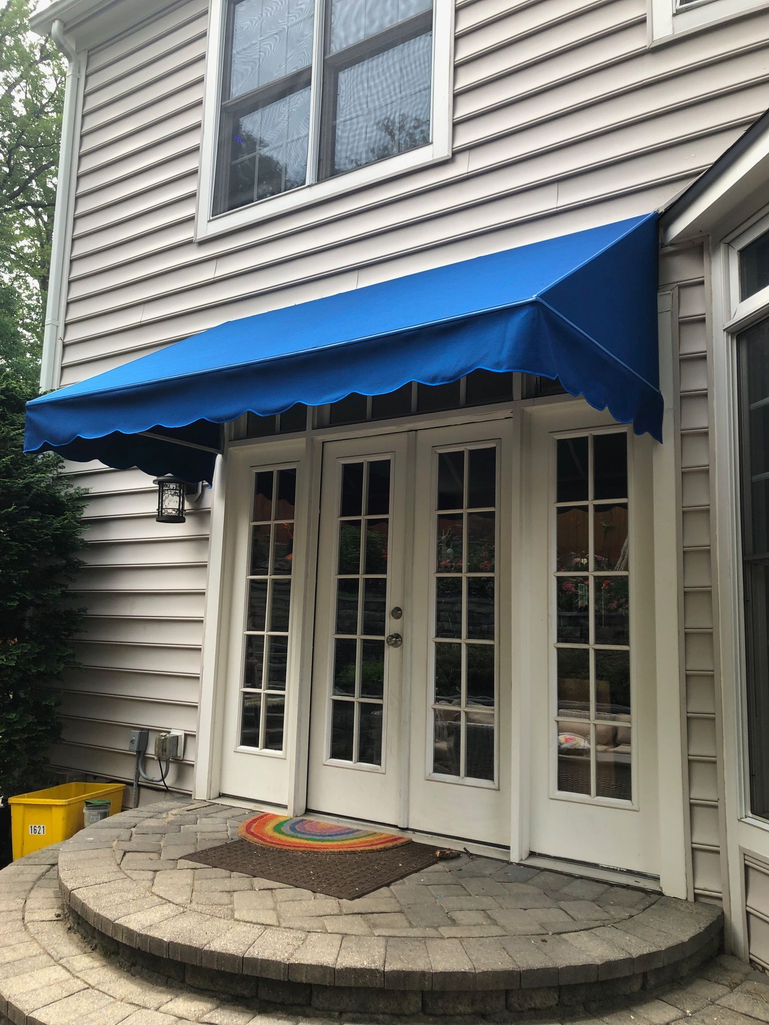 Blue awning over white double French doors on a stone patio outside a house.