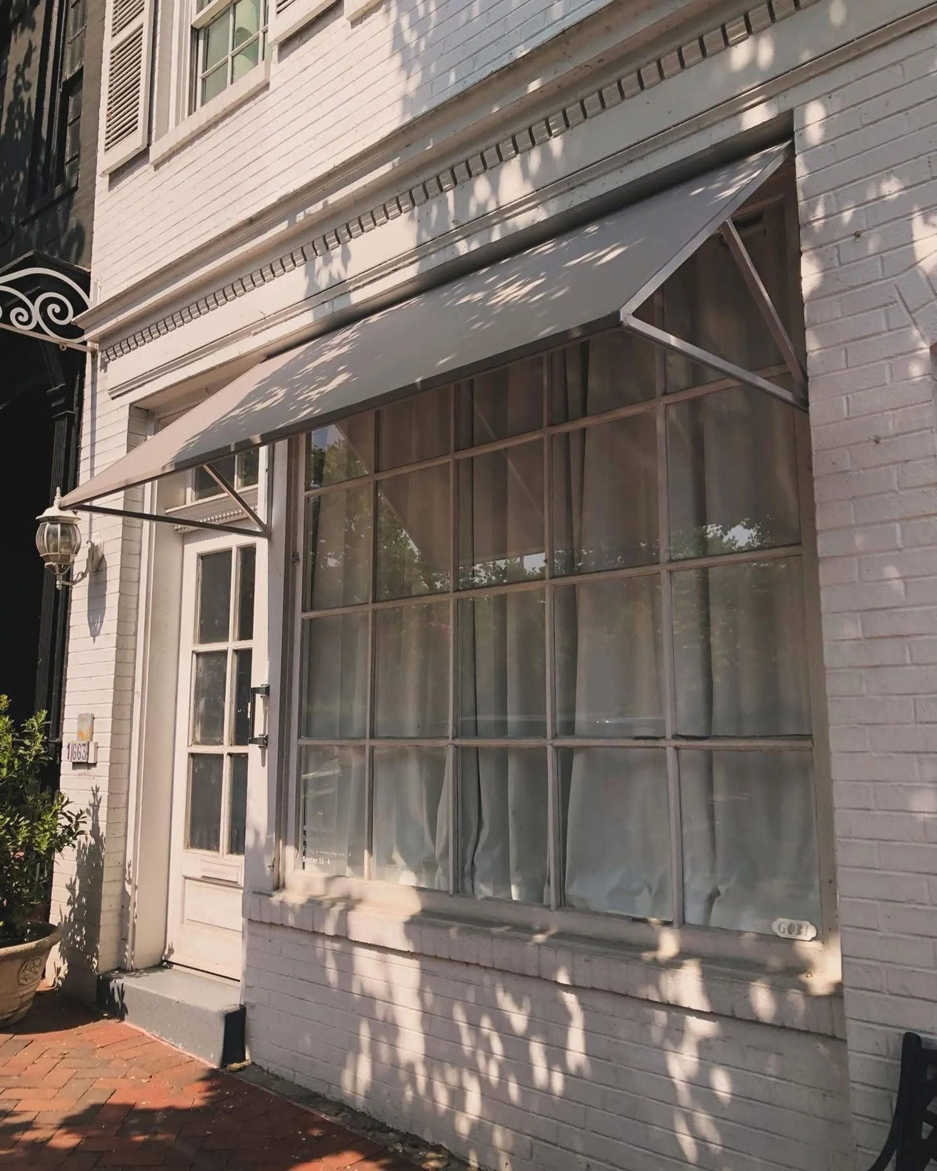 White brick storefront with large window, striped awning, and dappled sunlight on the facade