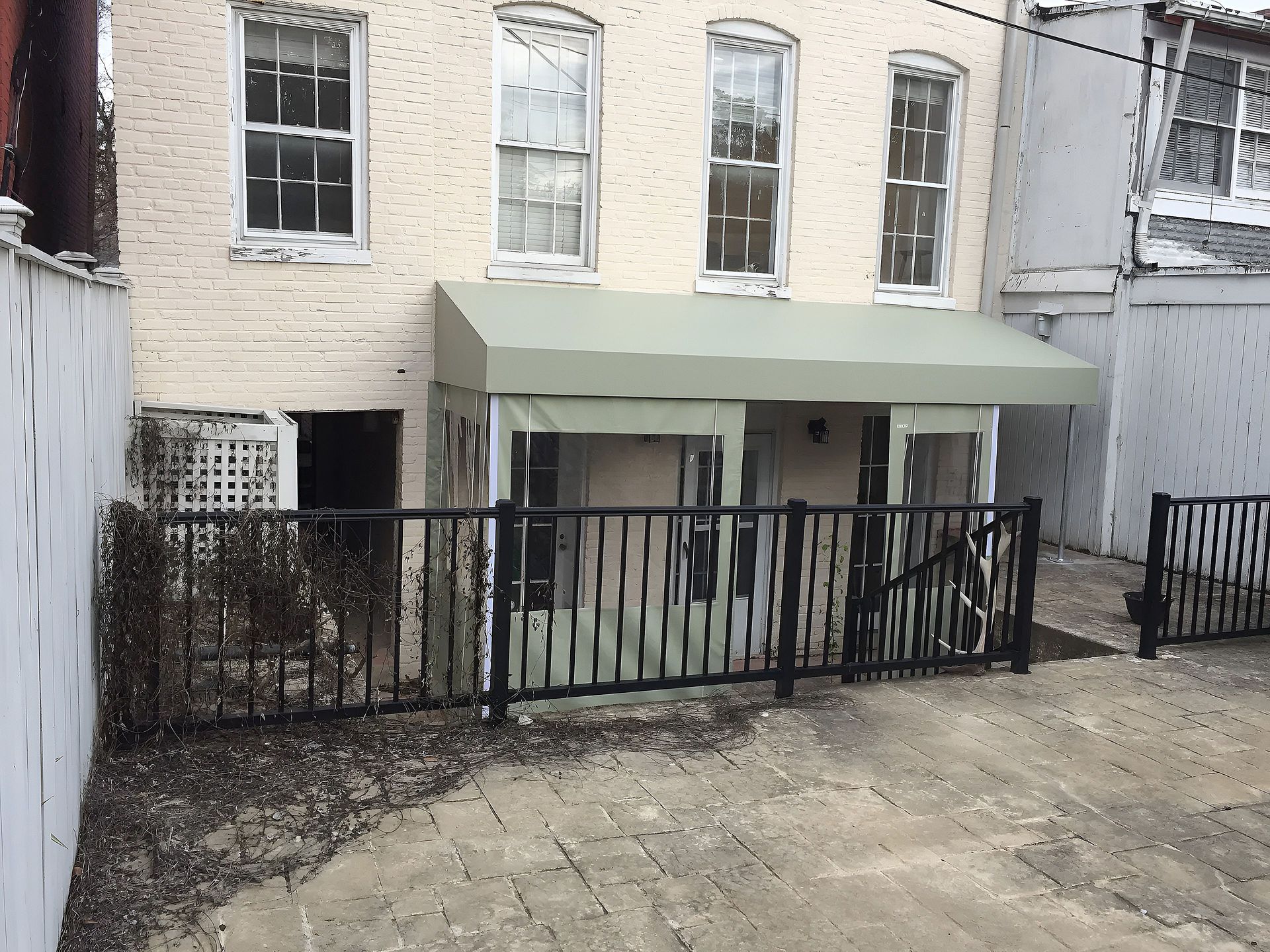 Brick townhouse rear patio with black fence and green awning over a lower door.