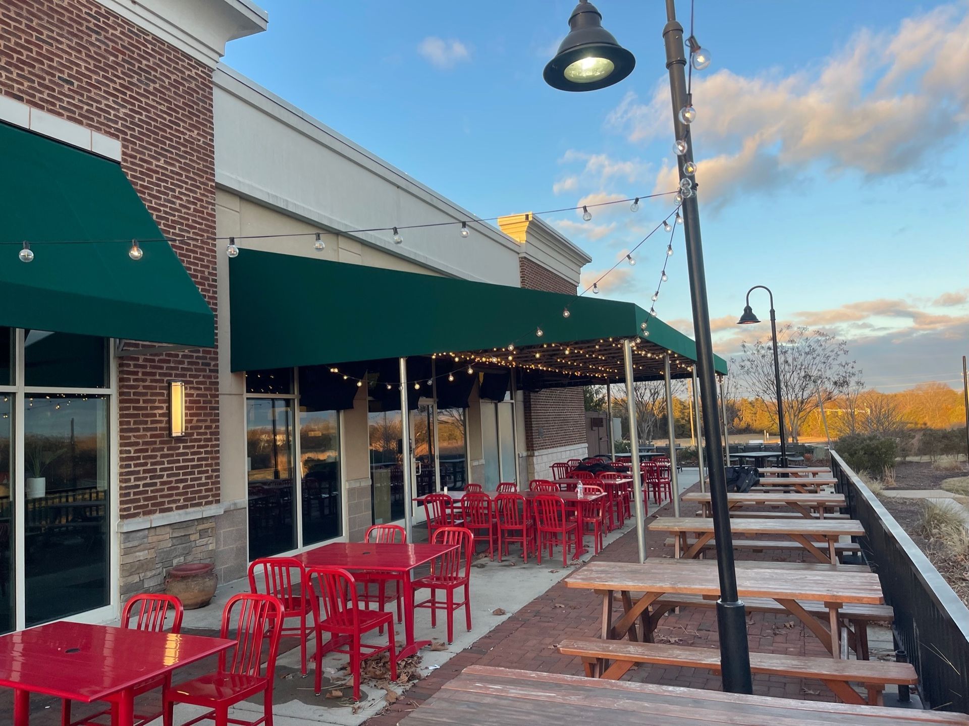 Outdoor restaurant patio with red tables and chairs under green awnings at sunset.