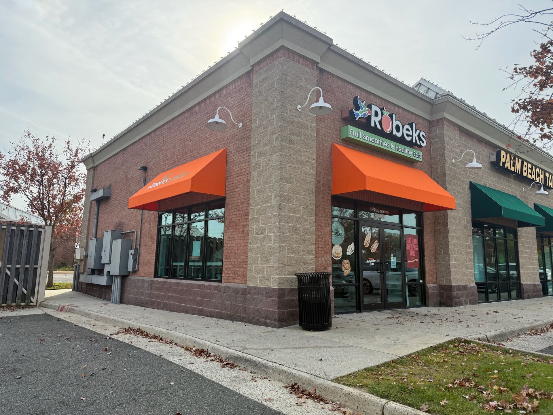 Corner brick storefront with orange awnings and glass windows on a cloudy day.