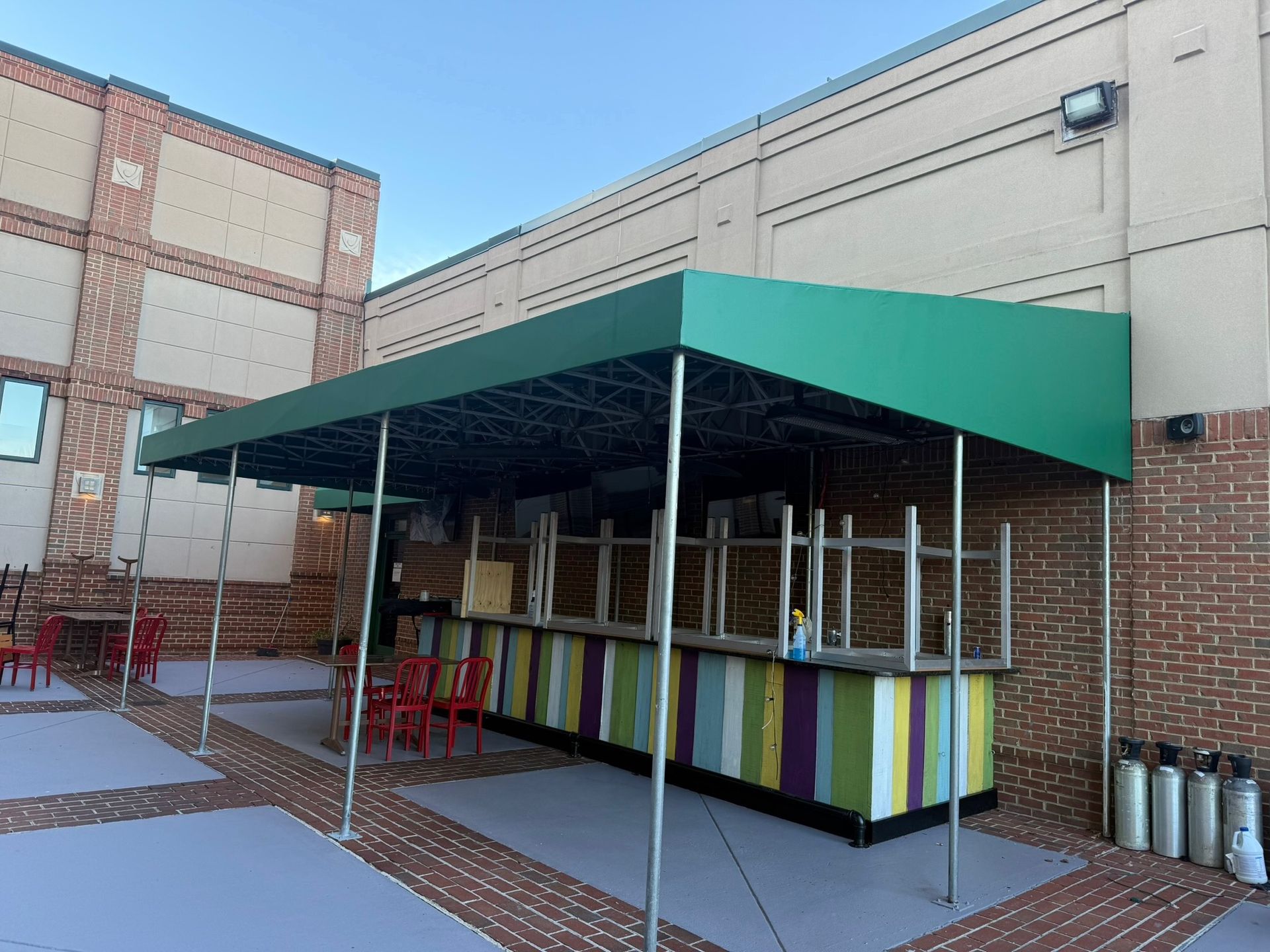 Outdoor school courtyard with a teal canopy over a colorful serving kiosk and tables.
