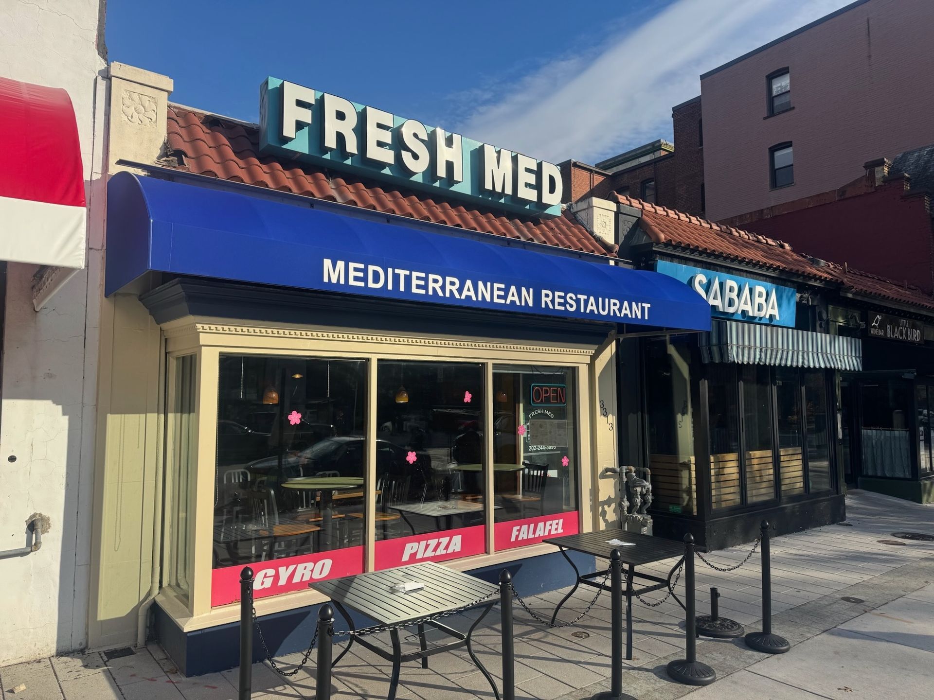 Storefront of Fresh Med Mediterranean Restaurant with blue awning and outdoor seating on a city street.