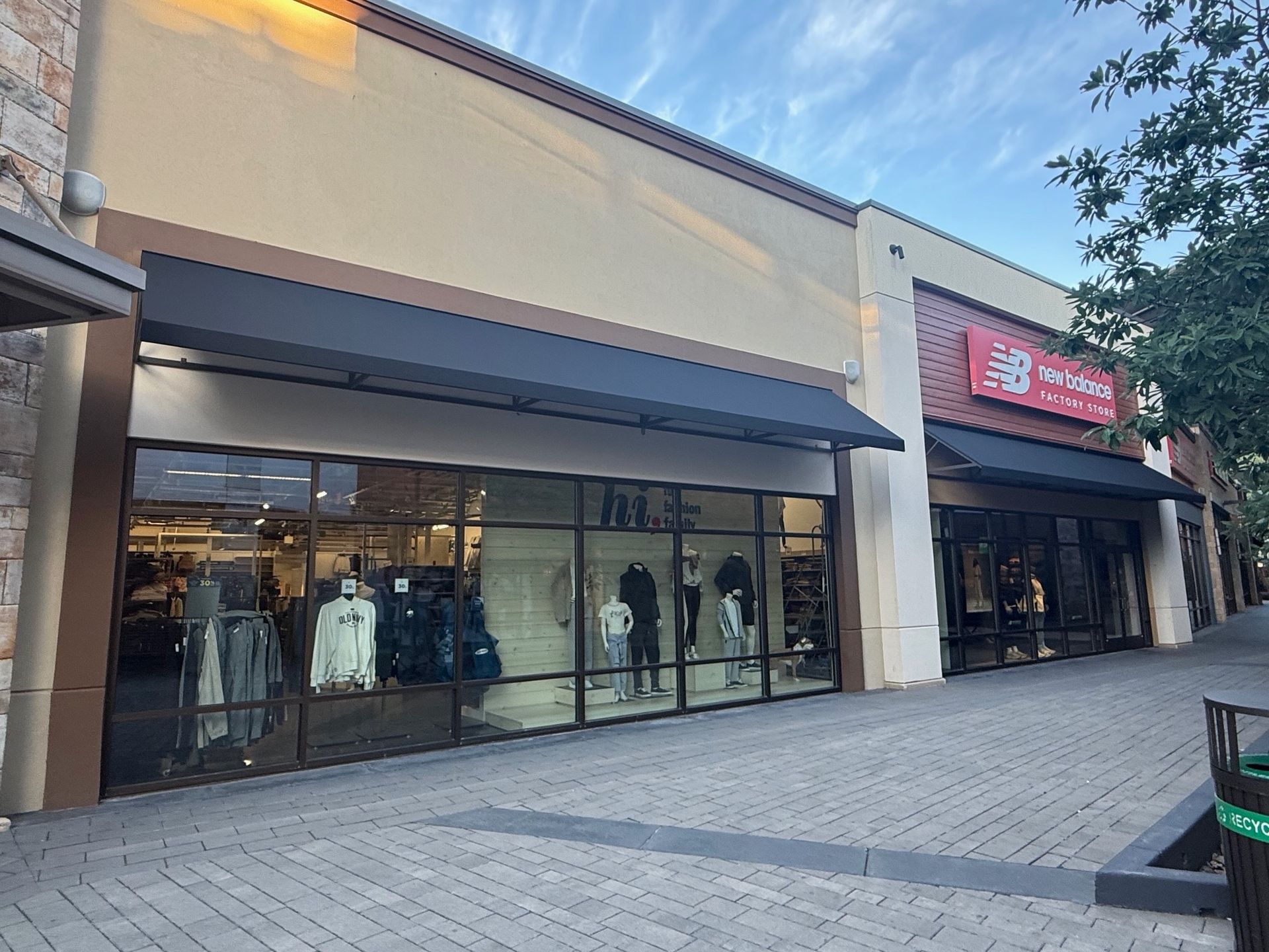 Storefronts with large windows and awnings along a quiet outdoor shopping walkway.