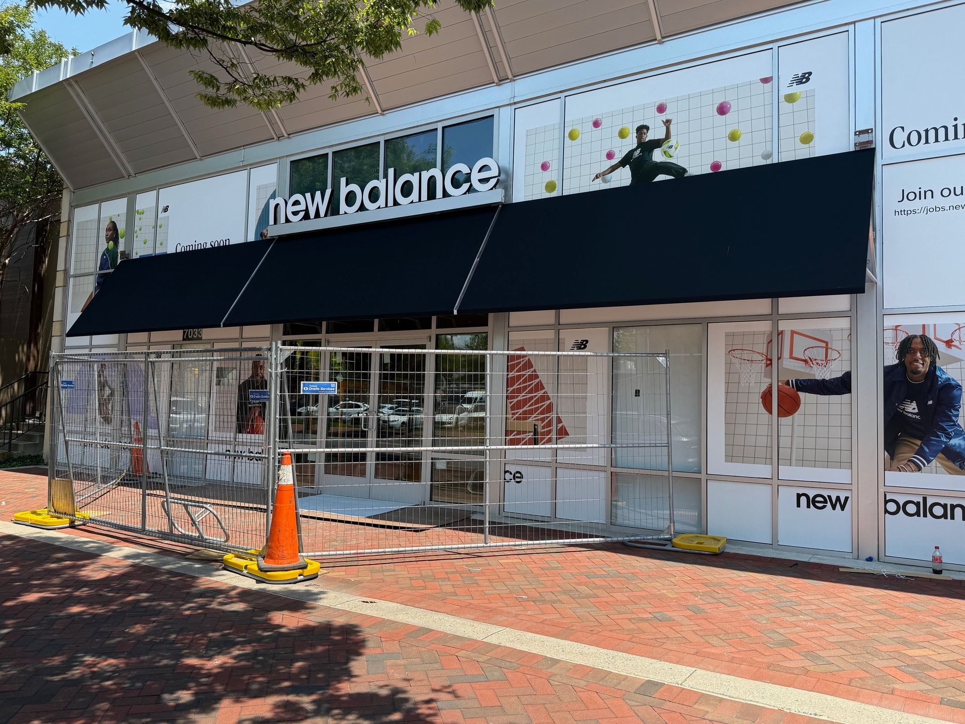 Storefront with a black awning and New Balance signage, viewed from a brick sidewalk.