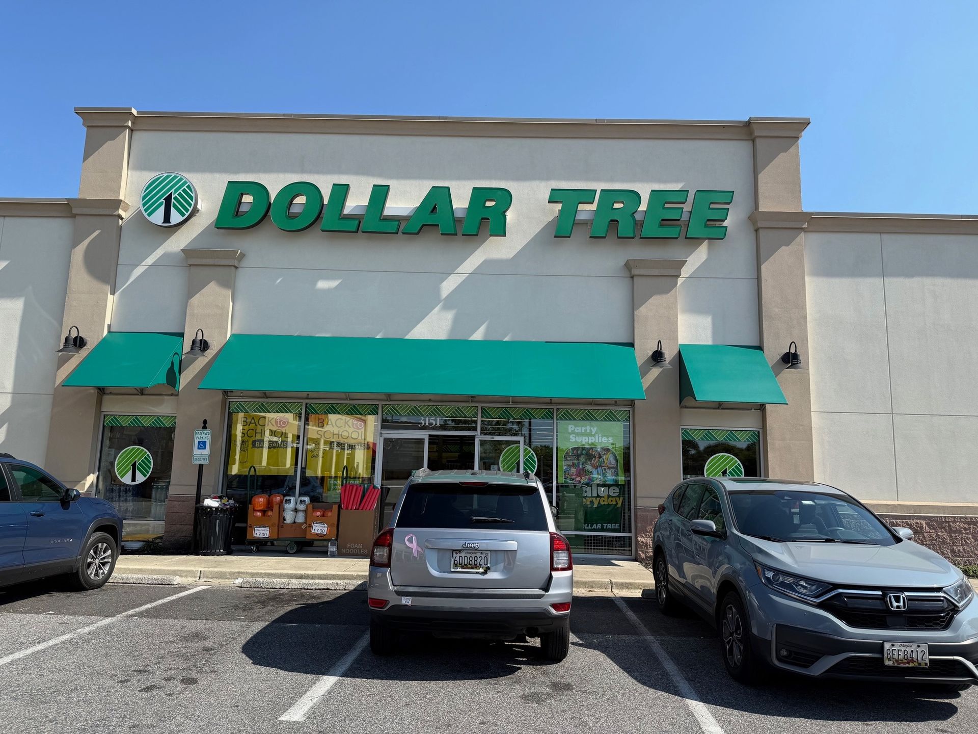 Dollar Tree storefront with green awnings and parked cars in front.