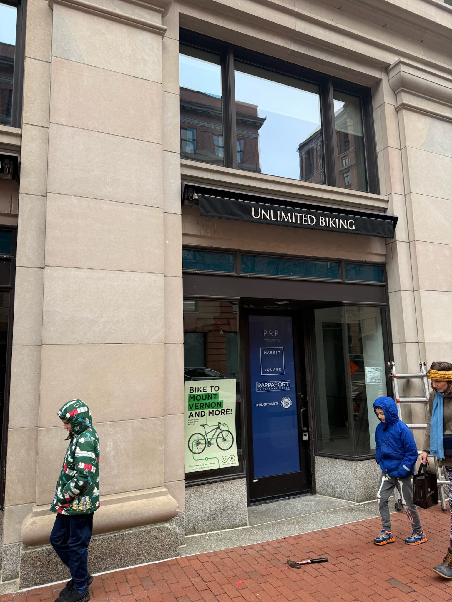 Storefront entrance with two people standing outside, one in green and one in blue hoodie.