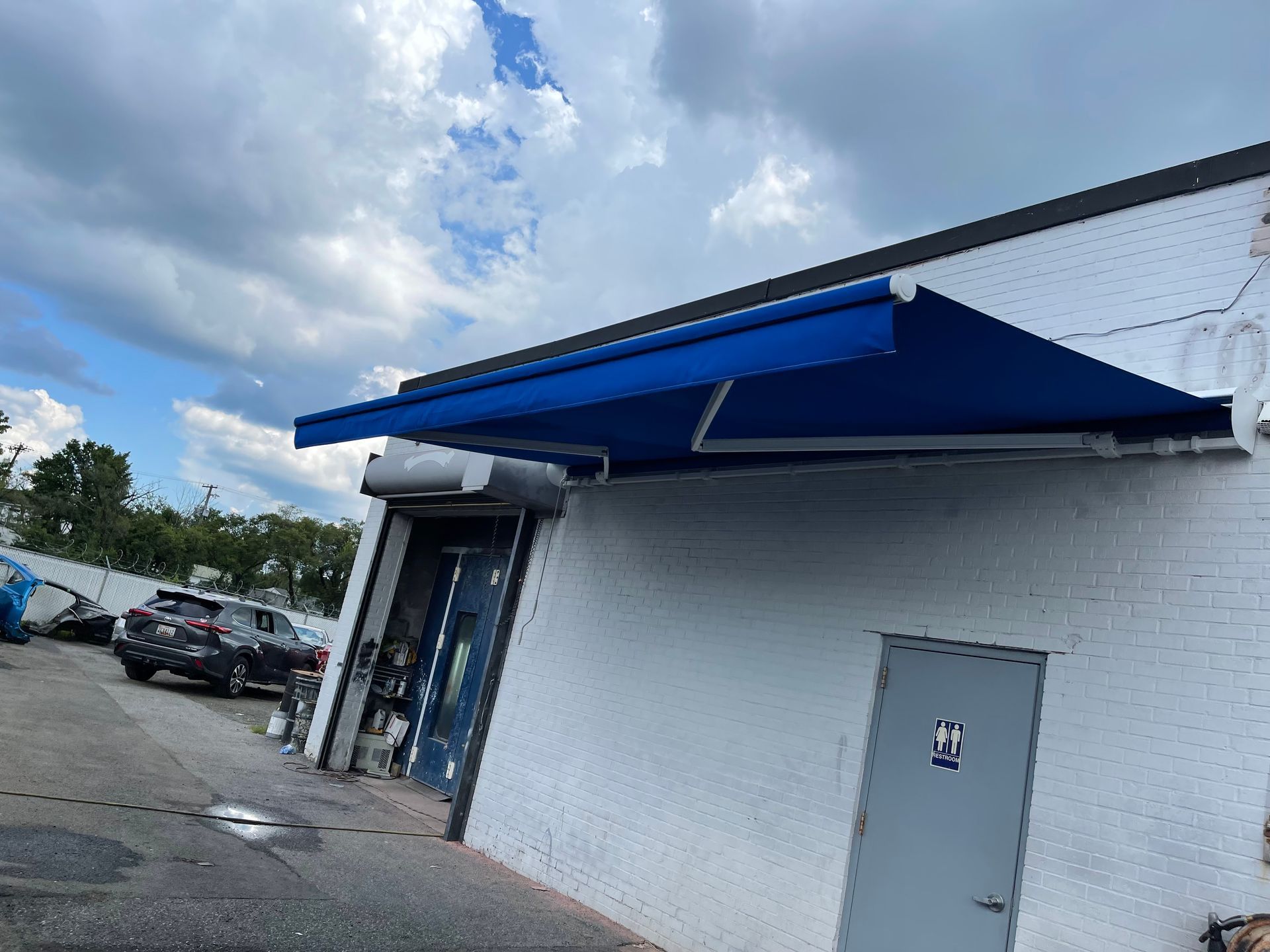 White brick storefront with blue awning and parked cars under a cloudy sky.