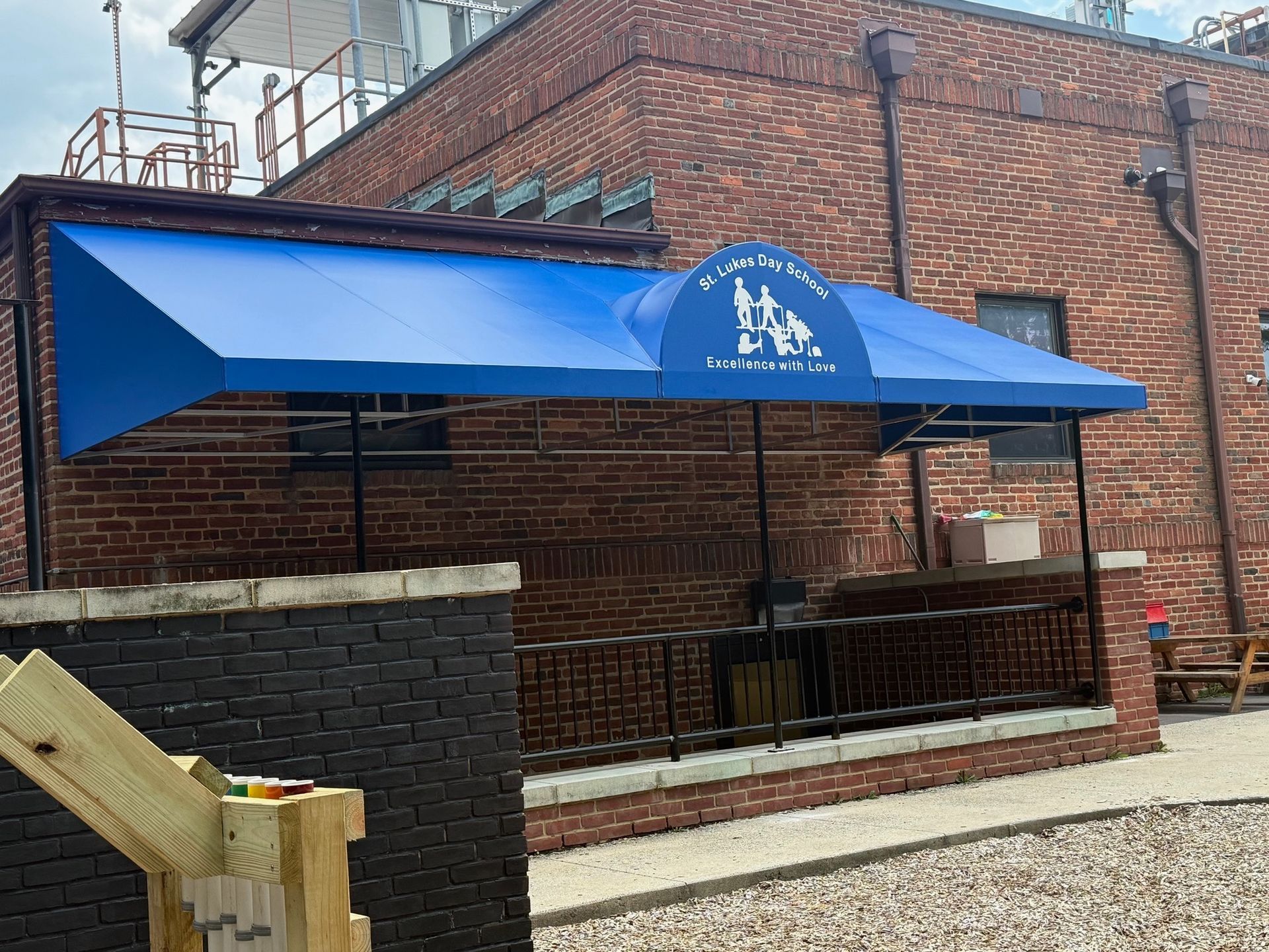 Blue canopy tent beside a brick building, with an outdoor seating area on a paved patio.