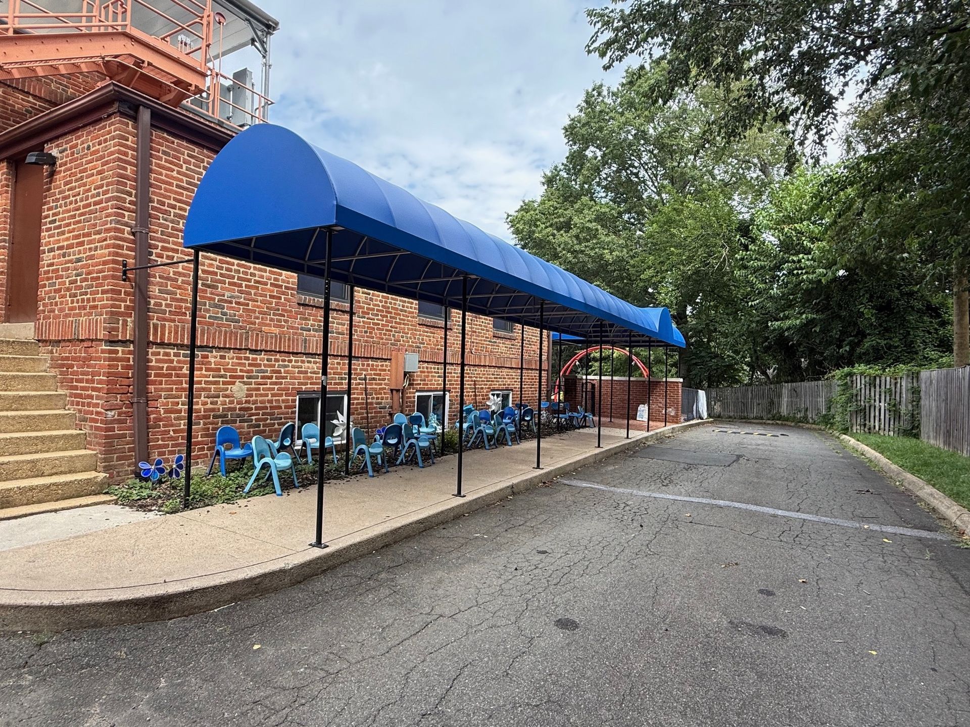 Blue awning covers outdoor seating beside a brick building on a wet pavement driveway.