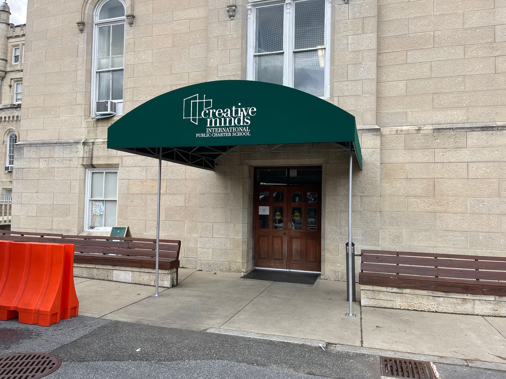 Stone building entrance with dark green awning, wooden door, and benches along the wall.