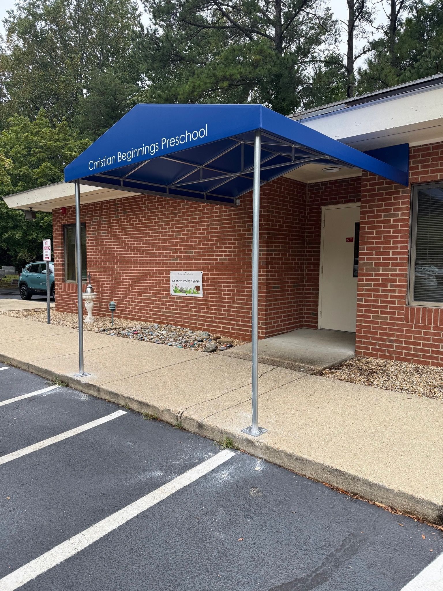 Blue awning over a brick building entrance with a wheelchair-accessible ramp and parking spaces nearby.