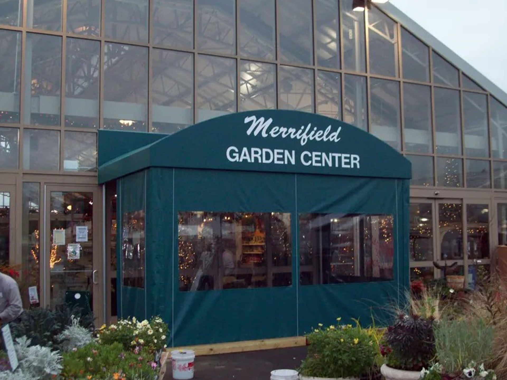 Merrifield Garden Center storefront with teal awning and glass entrance in a greenhouse setting