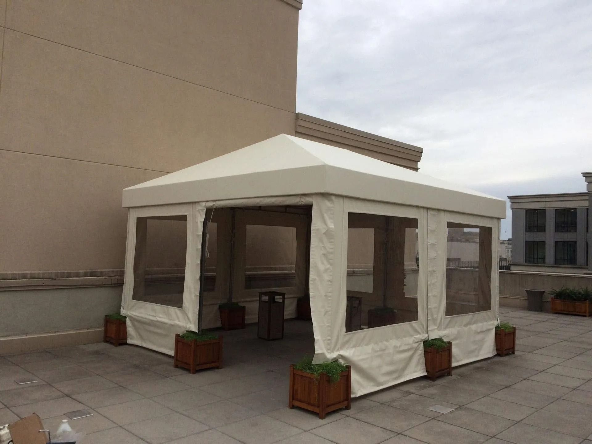 White outdoor canopy tent on a rooftop patio with potted plants and large window panels