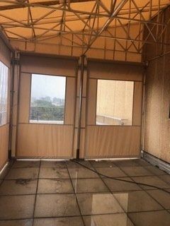 Empty enclosed patio with tan walls, metal roof trusses, and large windows overlooking a hazy view.