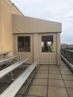 Rooftop walkway with beige siding, benches, and two small windows overlooking a city view