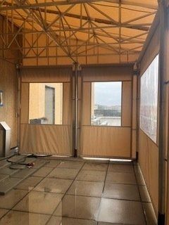 Empty sunroom with tan walls, tiled floor, and large windows showing a distant landscape.