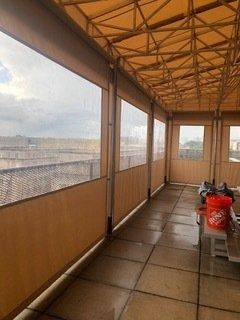 Covered terrace with tiled floor, wood-paneled walls, and a view through plastic screening.
