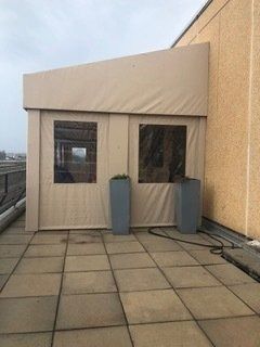Rooftop terrace with a beige tent-like structure and two small planters on a tiled floor.