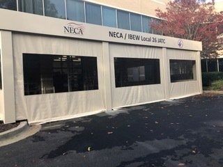 White NECA/IBEW Local 25 tent booth with black windows set up on pavement outdoors