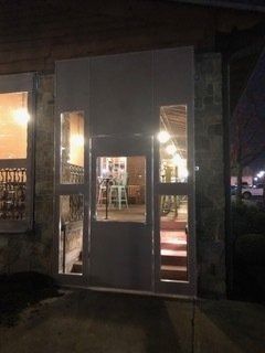 Dimly lit storefront entrance with a glass door and windows, showing a lit interior beyond.