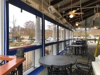 Empty outdoor café patio with tables, blue railing, and windows overlooking a park