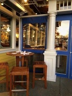 Outdoor café table and stools beside blue storefront windows and a white column