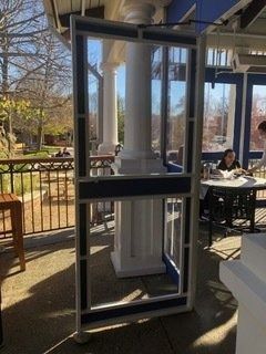 Glass-enclosed vertical lift on an outdoor restaurant patio beside tables and railings