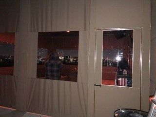 Person standing by a window in a dim room, looking out at a nighttime city view.