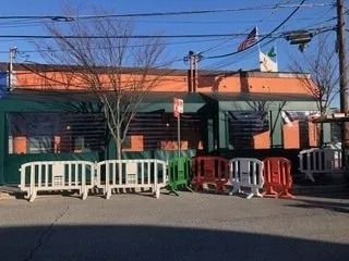 Street view of a building with green and orange facade, white and red barriers, and a Mexican flag overhead