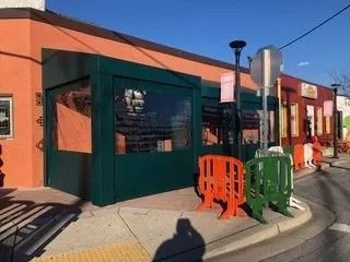 Orange storefront with green awning, orange and green barricades, and a curbside sidewalk on a sunny street
