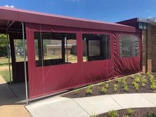 Maroon outdoor tent with clear windows beside a concrete walkway and landscaped plants