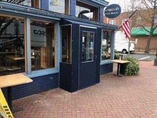 Small blue storefront with outdoor wooden tables and an American flag on a brick sidewalk