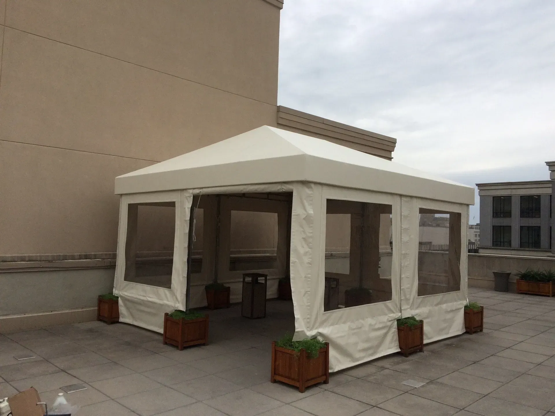 White canopy tent on a rooftop patio with potted plants and city buildings in the background