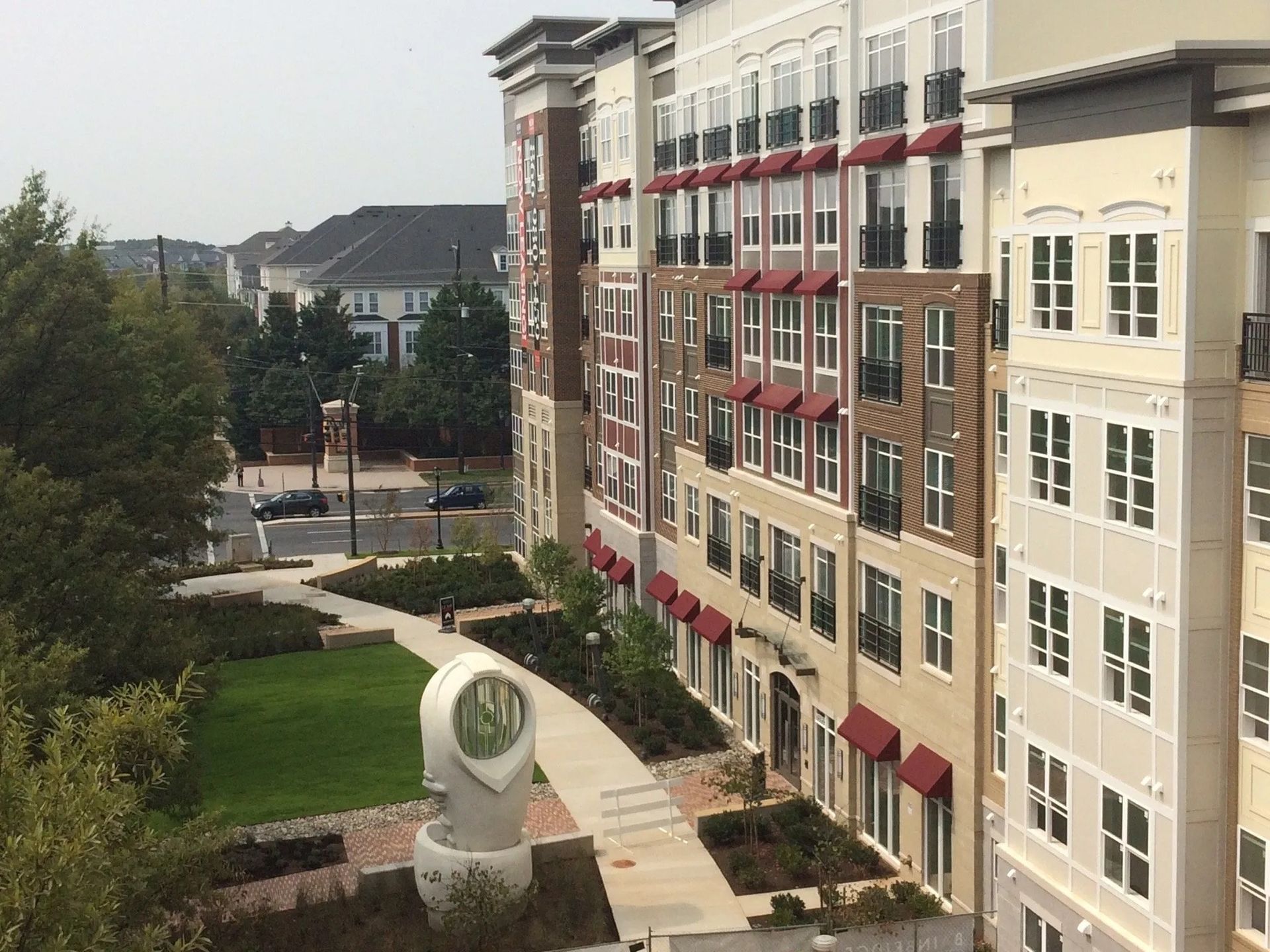 Apartment building courtyard with walkway, green lawn, and a stone sculpture