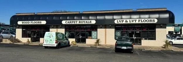 Strip mall storefronts with dark awnings and parked cars in front.